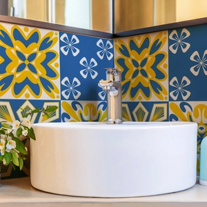 Mediterranean blue and yellow floral ceramic wall tiles behind a white cylindrical pedestal sink