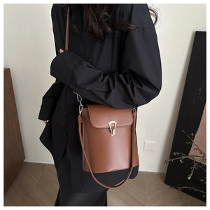 Sac seau en cuir marron avec boucle dorée porté par un mannequin en décor urbain