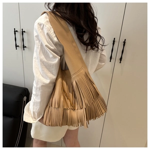 Detail of beige pebbled leather shoulder bag featuring long bohemian tassels and soft texture