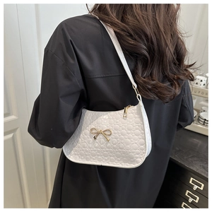 Détail d'un sac sous le bras en cuir verni blanc matelassé avec nœud doré et fermeture éclair