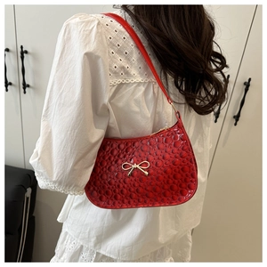Detail of red bubble-textured shoulder bag with a gold bow accent on white lace outfit
