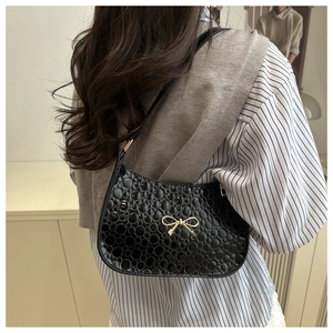 Back view of model wearing a black glossy patent leather shoulder bag with a gold bow