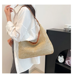 Detail of hollow woven straw hobo bag with brown leather straps worn by a model
