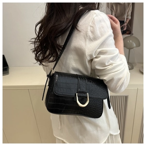 Détail du sac baguette noir texture crocodile avec boucle fer à cheval dorée porté