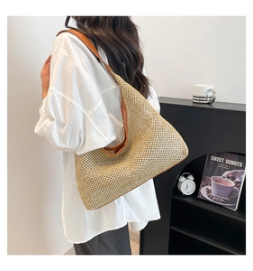 Detail of a woven straw beach bag with brown leather handles worn by a model
