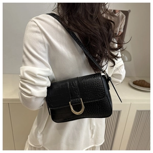 Détail d'un sac bandoulière noir effet crocodile avec boucle dorée sur fond blanc