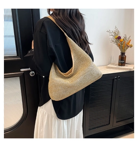 Detail of hand-woven straw tote bag with wide shoulder strap worn by a female model