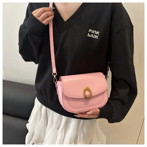 Détail d'un sac besace en cuir rose avec boucle dorée porté à l'épaule par un mannequin
