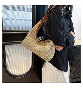 Detail of woven straw shoulder bag featuring brown leather trim and large moon-shaped design
