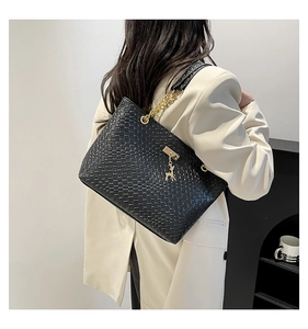 Detail of black woven tote bag with gold deer pendant and chain strap worn by a model