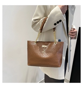 Detail of brown woven tote bag with gold elk charm and metallic chain strap
