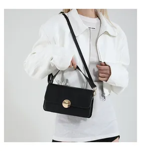 Détail d'un petit sac bandoulière noir minimaliste en cuir avec boucle ronde dorée sur modèle