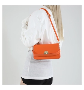 Détail d'un sac bandoulière orange en cuir avec boucle dorée ronde sur une tenue blanche