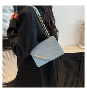 Detail of light blue crossbody bag featuring woven texture and gold chain strap
