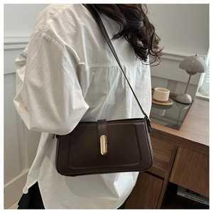 Detail of minimalist dark brown shoulder bag with golden metallic buckle in a cozy setting