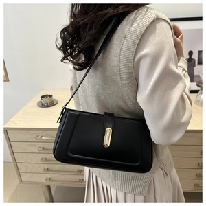 Detail of a black minimalist baguette shoulder bag with an elegant gold oval buckle