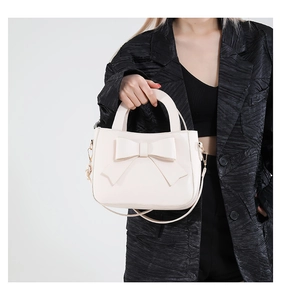 Detail of cream crossbody bag with large bow and gold hooks held by model in black blazer