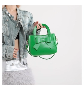 Detail of bright green handbag with bow decoration, PU leather and golden hardware