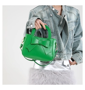 Detail of green handbag with a large leather bow and golden metal hardware
