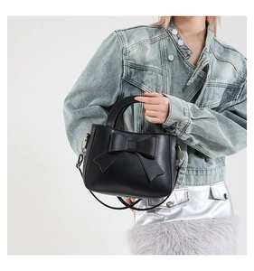 Detail of a black crossbody bag with a large bow decoration and gold metal hooks