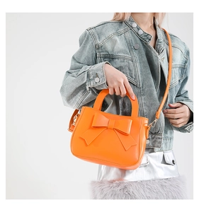 Detail of bright orange square bag featuring a large bow and adjustable shoulder strap