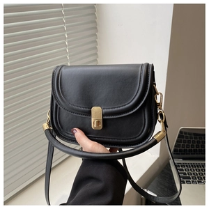 Detail of minimalist black saddle bag with gold metal lock and elegant stitching