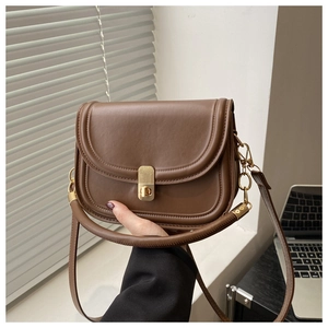 Detail of a brown leather saddle bag featuring a gold metal clasp and dual strap options