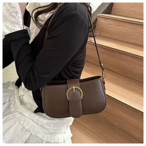 Détail d'un sac bandoulière marron mat avec une grande boucle fer à cheval dorée rétro
