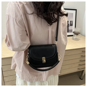 Detail of minimalist black leather crossbody bag featuring gold metal clasp and dual straps