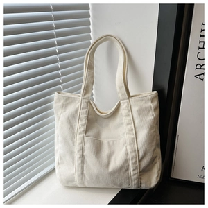 Detail of off-white corduroy tote bag showing front pocket and soft texture