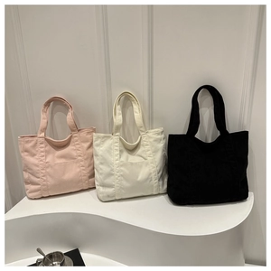 Detailed texture of corduroy tote bags in pink, beige, and black on a minimalist display
