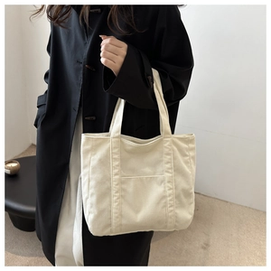 Detail of off-white corduroy tote bag showing vertical ribbed texture and front pocket