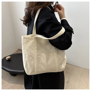 Detail shot of a cream corduroy tote bag showing its ribbed texture and spacious front pocket