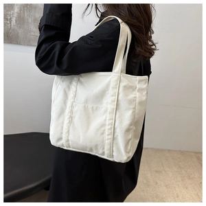 Close-up of off-white corduroy tote bag showing textured stripes and front pocket