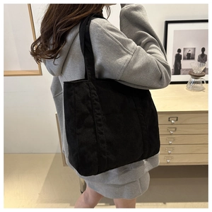 Detail of black corduroy tote bag showing vertical texture and wide shoulder strap