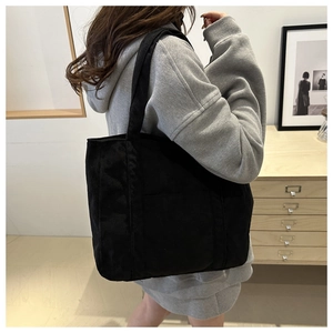 Detail view of the black corduroy tote bag showing its thick ribbed texture and handle