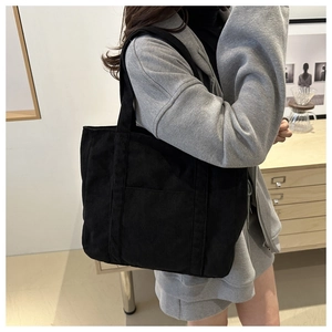 Detailed close-up of a black corduroy tote bag featuring a textured surface and large pocket