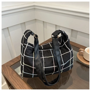 Detail of black nylon tote bag featuring colorful grid stitching and wide leather straps