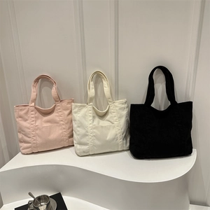 Three corduroy tote bags in pink, beige, and black displayed on a white stylish stand