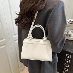 White leather tote bag with woven knot handle and gold lettering shown on model
