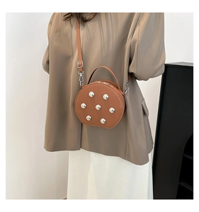 Detailed view of a brown round crossbody bag with silver rivets and leather texture