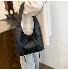 Detail view of large bow accent and silver brand logo on black leather tote bag