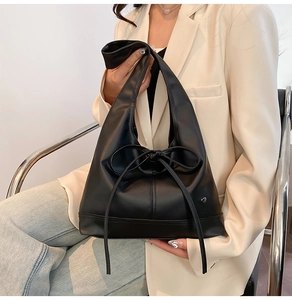 Detail of black leather hobo tote with bow accent, styled on woman in beige blazer
