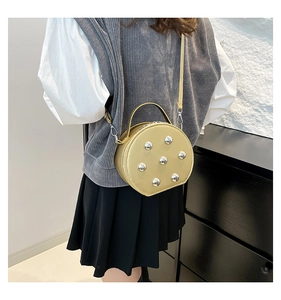 Vue latérale d'un petit sac rond jaune pâle avec des rivets argentés porté par un modèle