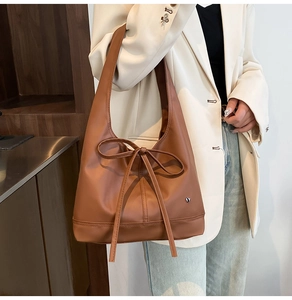 Detail of a brown PU leather shoulder bag with a long ribbon bow and silver heart logo