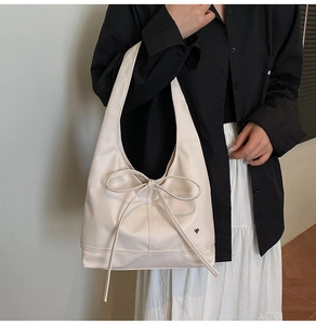 Detail of cream oversized tote bag featuring a large bow and metallic heart charm