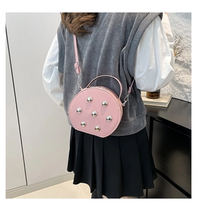 Detailansicht einer rosa runden Umhängetasche mit silbernen Nieten an einem Model