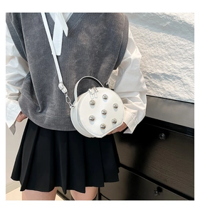 Détail d'un sac bandoulière rond blanc avec clous argentés et double fermeture éclair