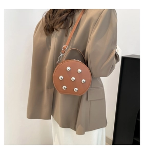 Detail of round brown crossbody bag with silver rivets held by a model in a brown blazer