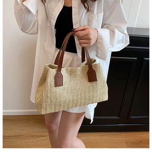 Close-up of a woven straw tote bag featuring brown leather handles and reinforced stitching